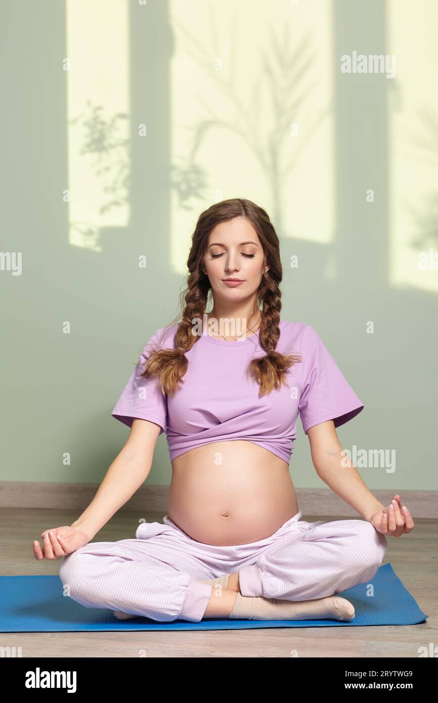 A pregnant woman sits crosslegged, meditating and practicing yoga for