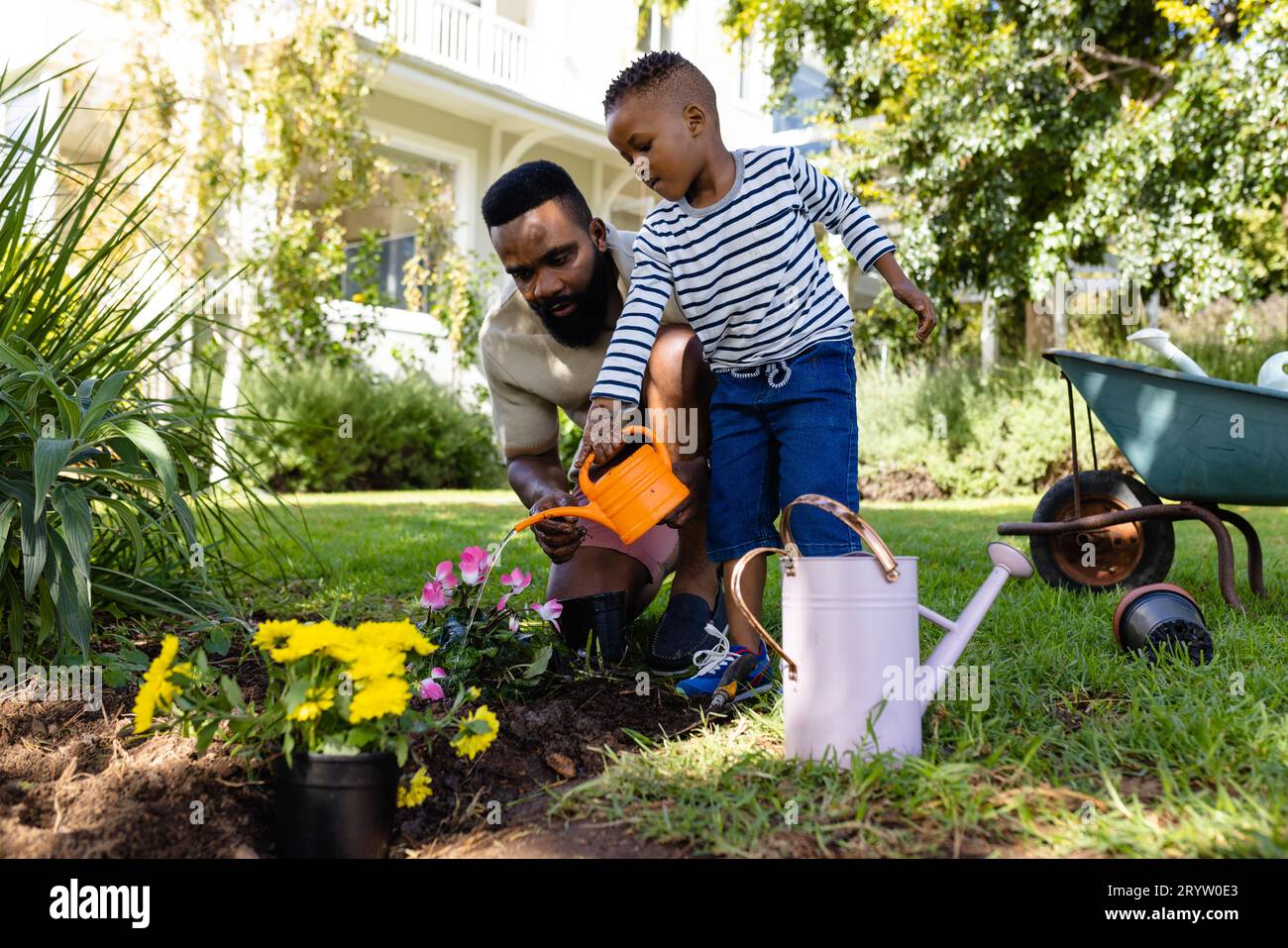 African american father with son watering flower pots and plants in ...