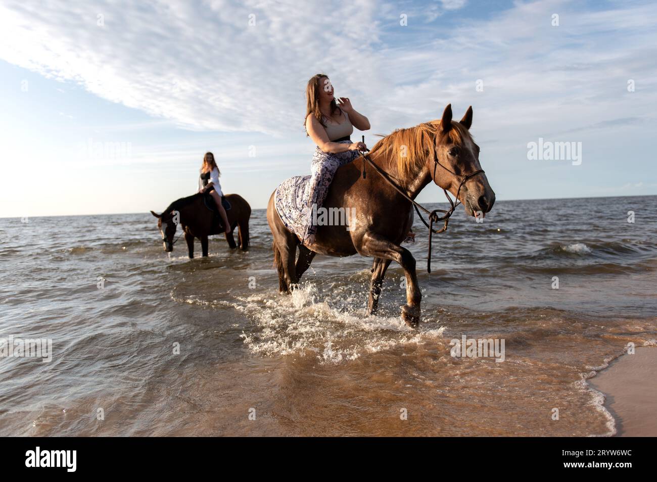 Two female riders on horseback in the surf of an ocean beach, with ...