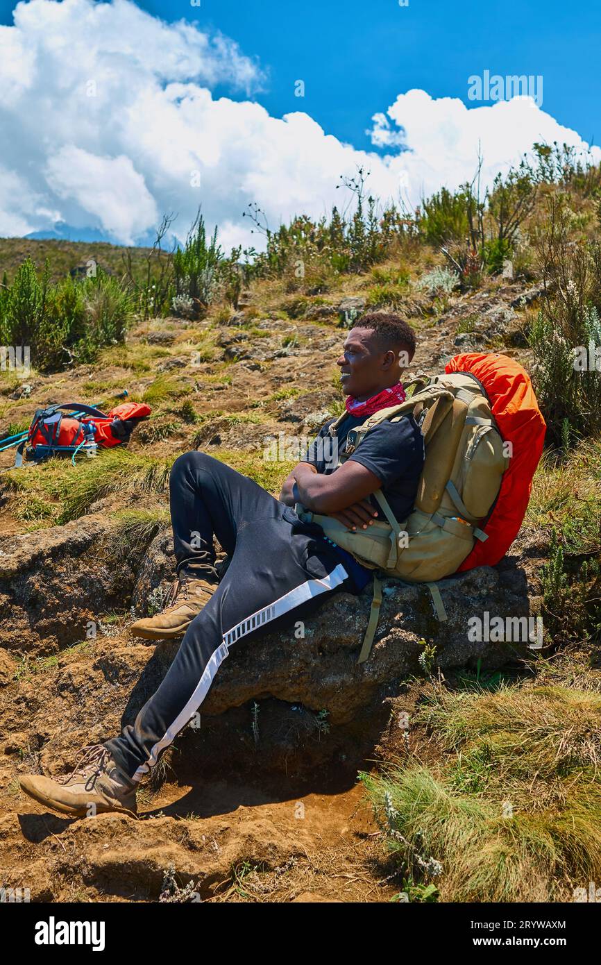a dark-skinned guy with a backpack is resting in the mountains Stock Photo