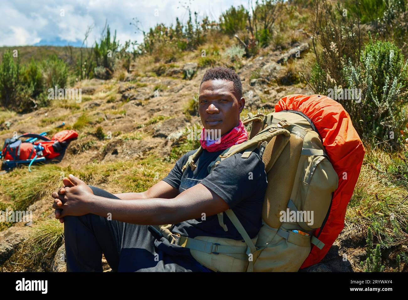 a dark-skinned guy with a backpack is resting in the mountains Stock Photo