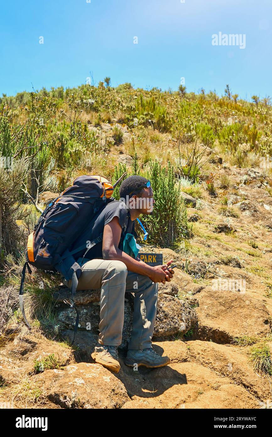 a dark-skinned guy with a backpack is resting in the mountains Stock Photo