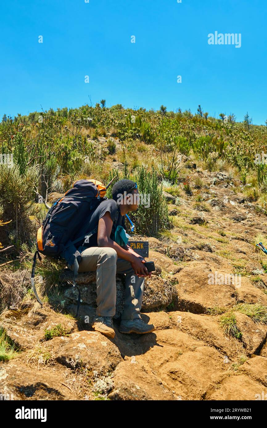 a dark-skinned guy with a backpack is resting in the mountains Stock Photo