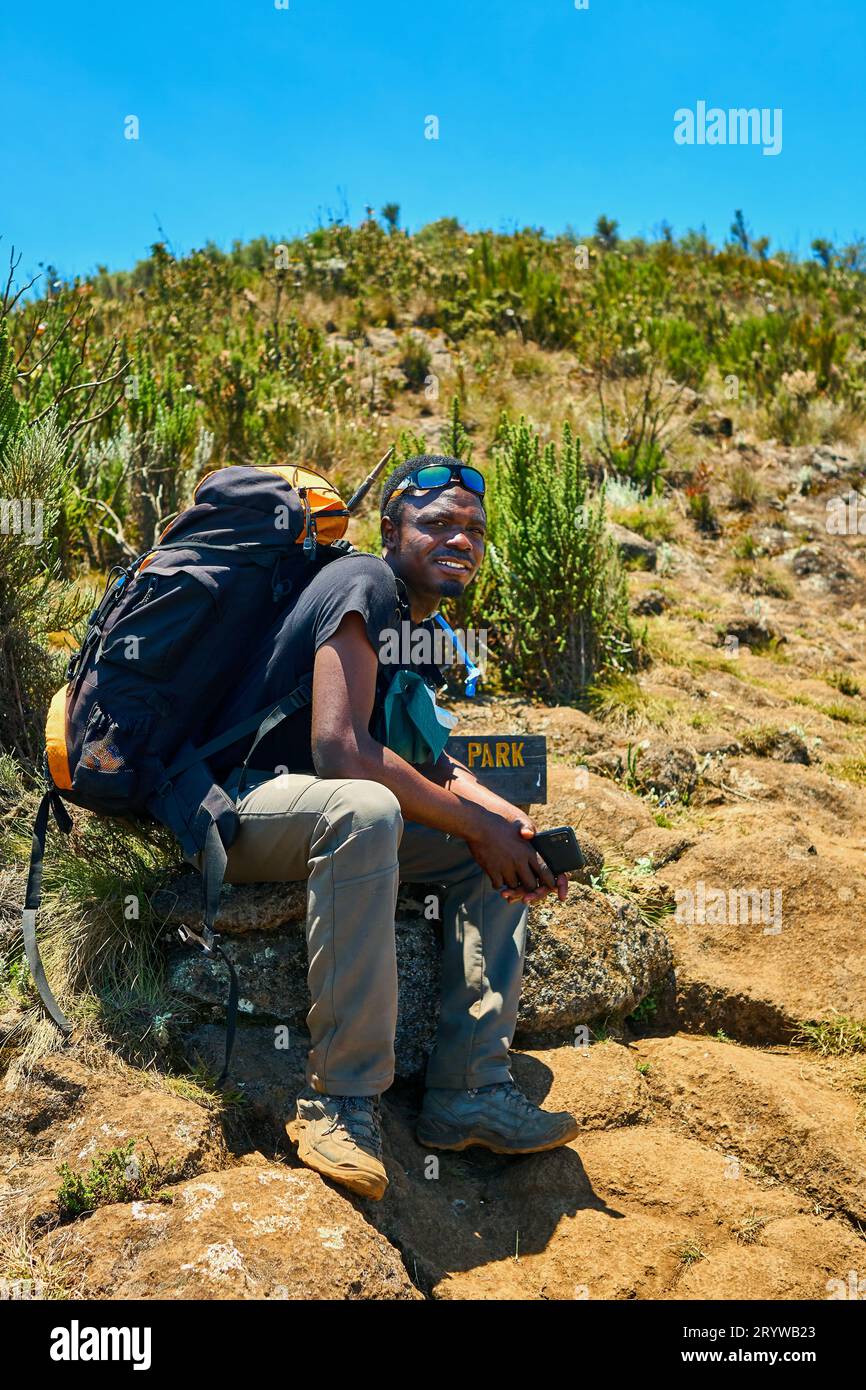 a dark-skinned guy with a backpack is resting in the mountains Stock Photo