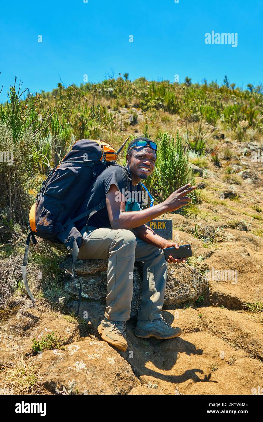 a dark-skinned guy with a backpack is resting in the mountains Stock Photo