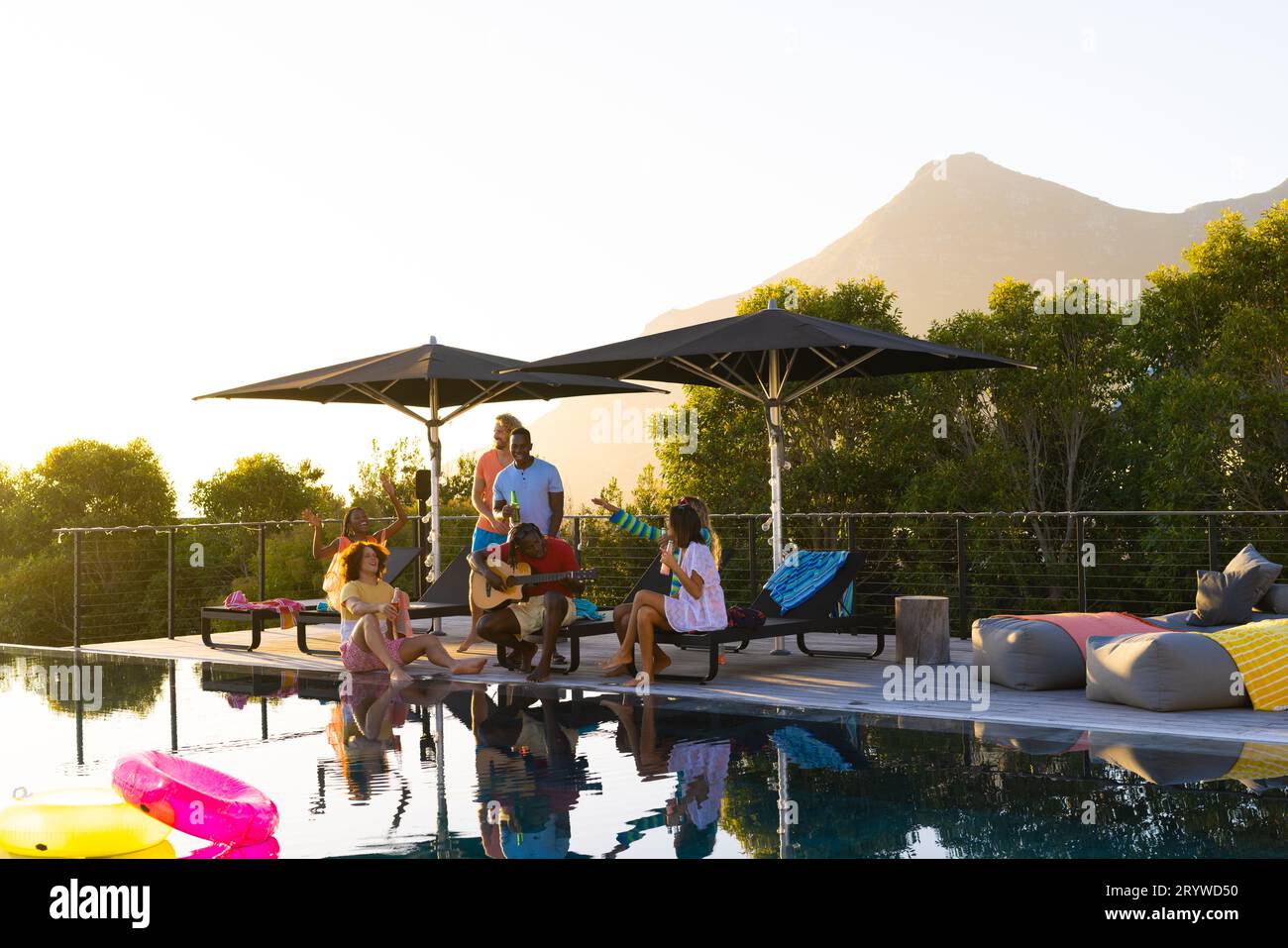 Happy diverse group of friends having pool party and playing guitar in ...
