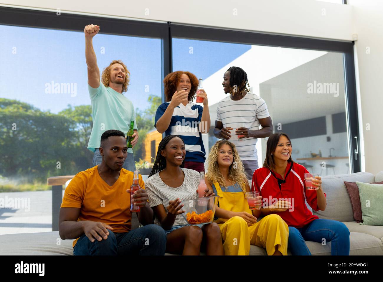Group of diverse friends sitting on sofa, watching sport on tv and cheering Stock Photo