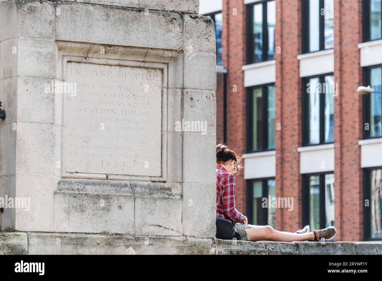 A women eats her lunch whilst sitting on a stone plinth outside Christ Church in Spitalfields, London, E1. Stock Photo