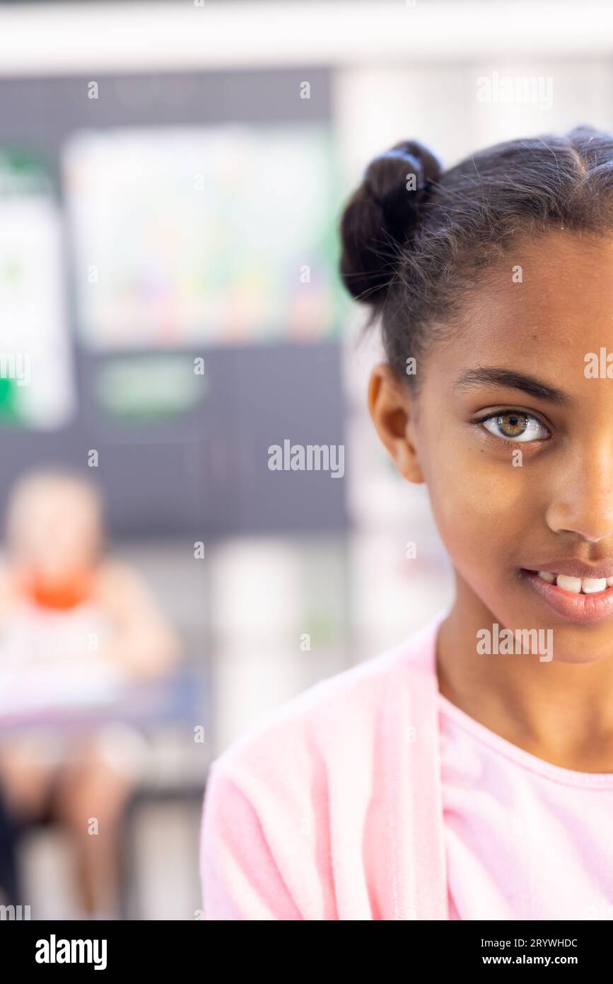 Vertical half face portrait of smiling biracial schoolgirl in classroom with copy space Stock Photo