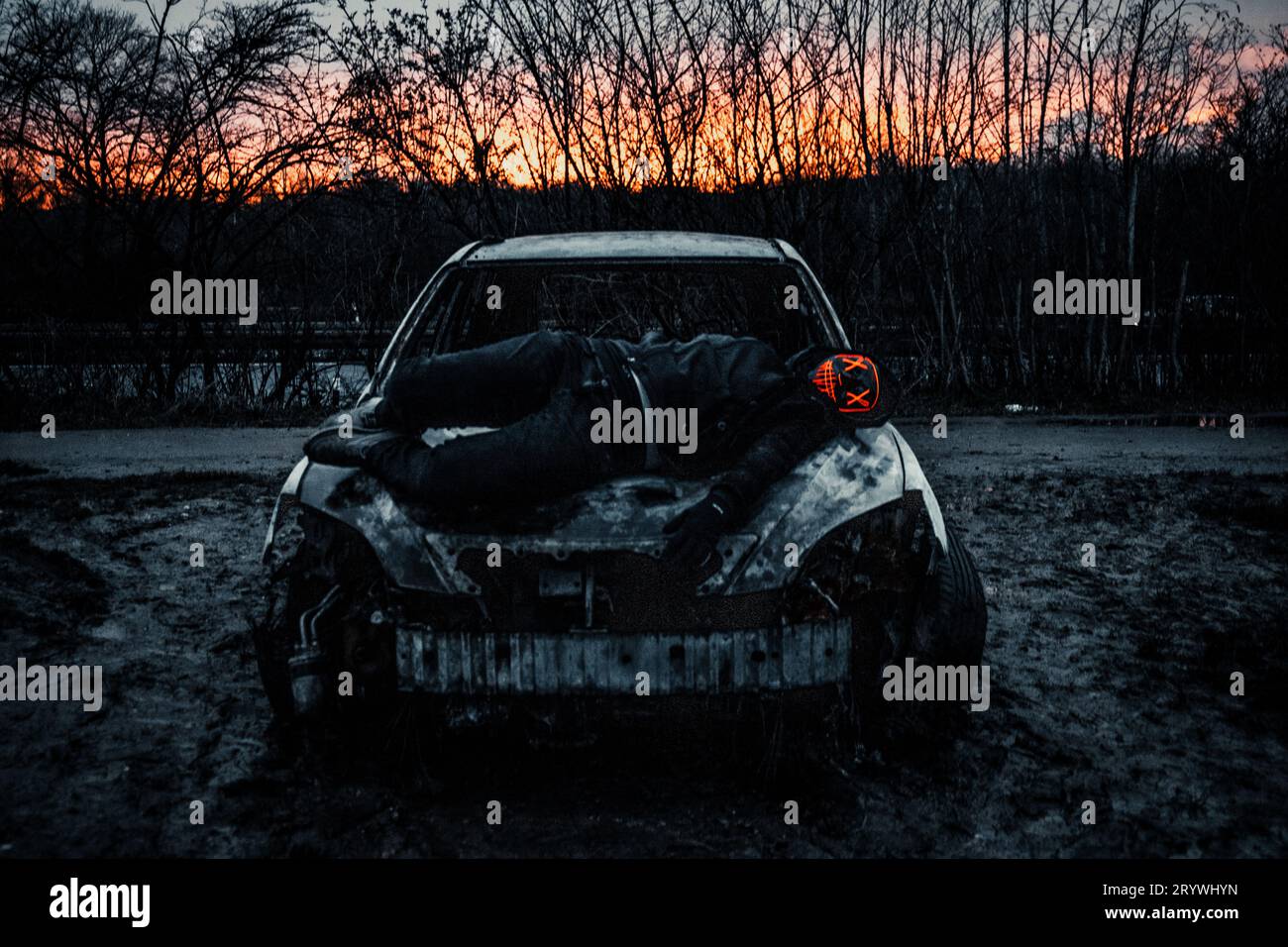 Destruction in the Night: Person with Purge Mask on a Burnt-Out Car Stock Photo