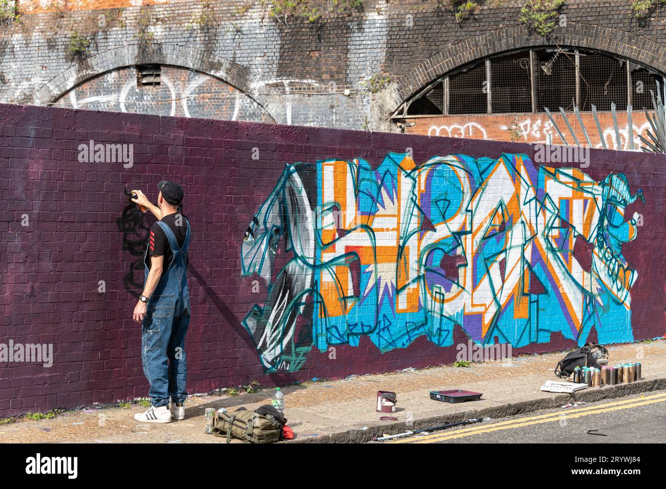 A graffiti artist spray paints a wall in Braithwaite St Shoreditch