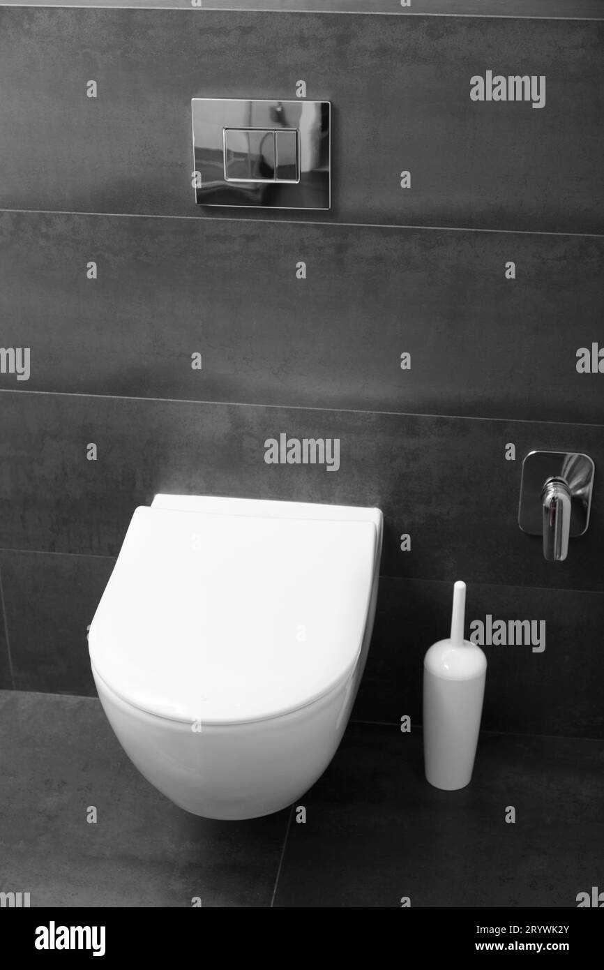 A modern wallmounted white toilet with a closed lid and a shiny chrome