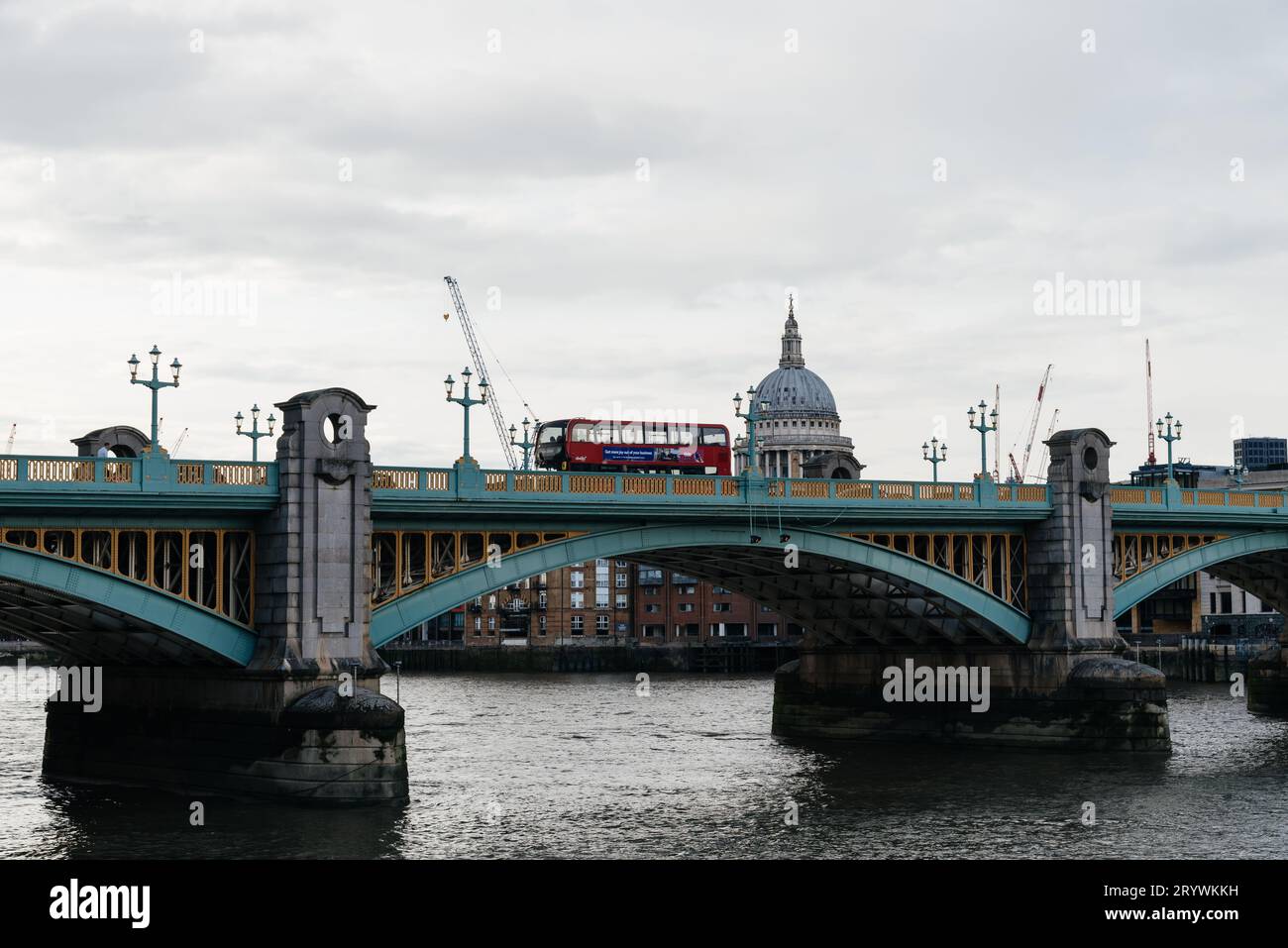 LONDON, UK - August 26, 2023: Red Bus crossing Southwark Bridge over Thames River against St Paul Cathedral in the City of London. View at dusk Stock Photo