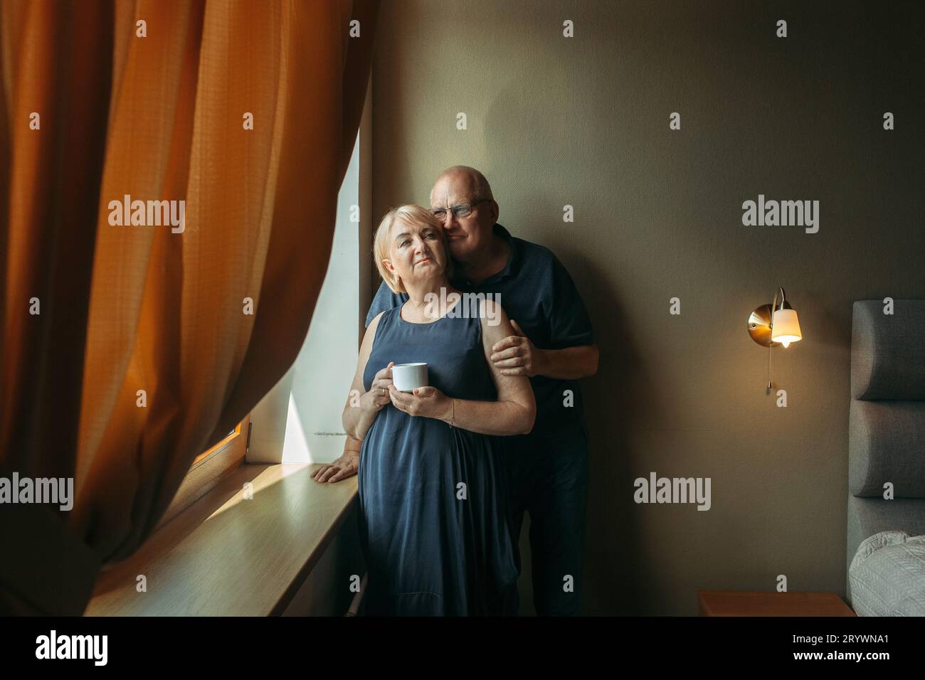Portrait of a married elderly couple standing at the window. The man ...