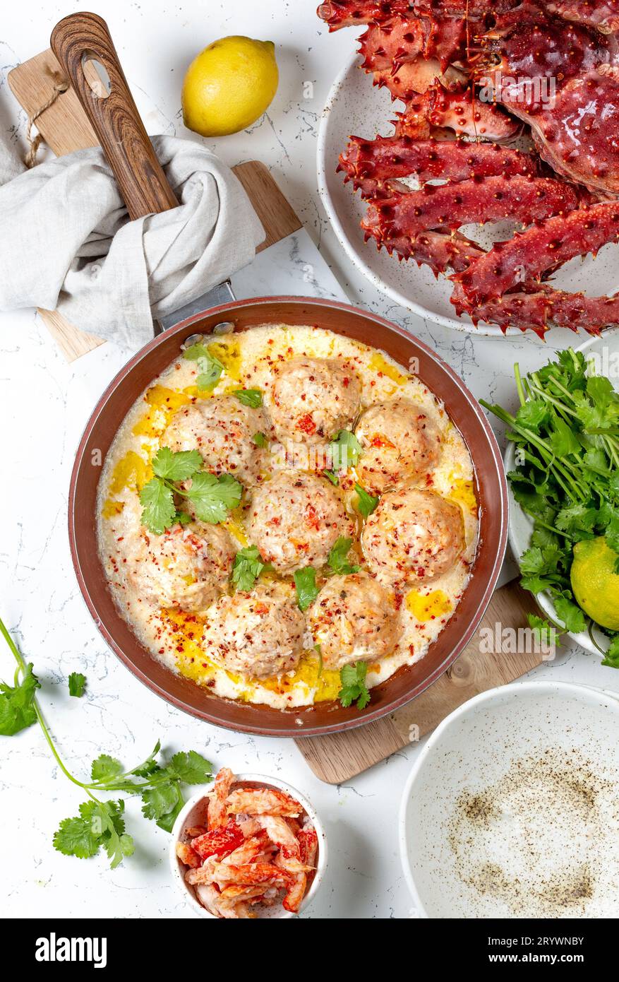 CRABMEATBALLS crab meatballs in white creamy sauce in red pan, whole king crab, cilantro, lemon and white wine on white backgrou Stock Photo