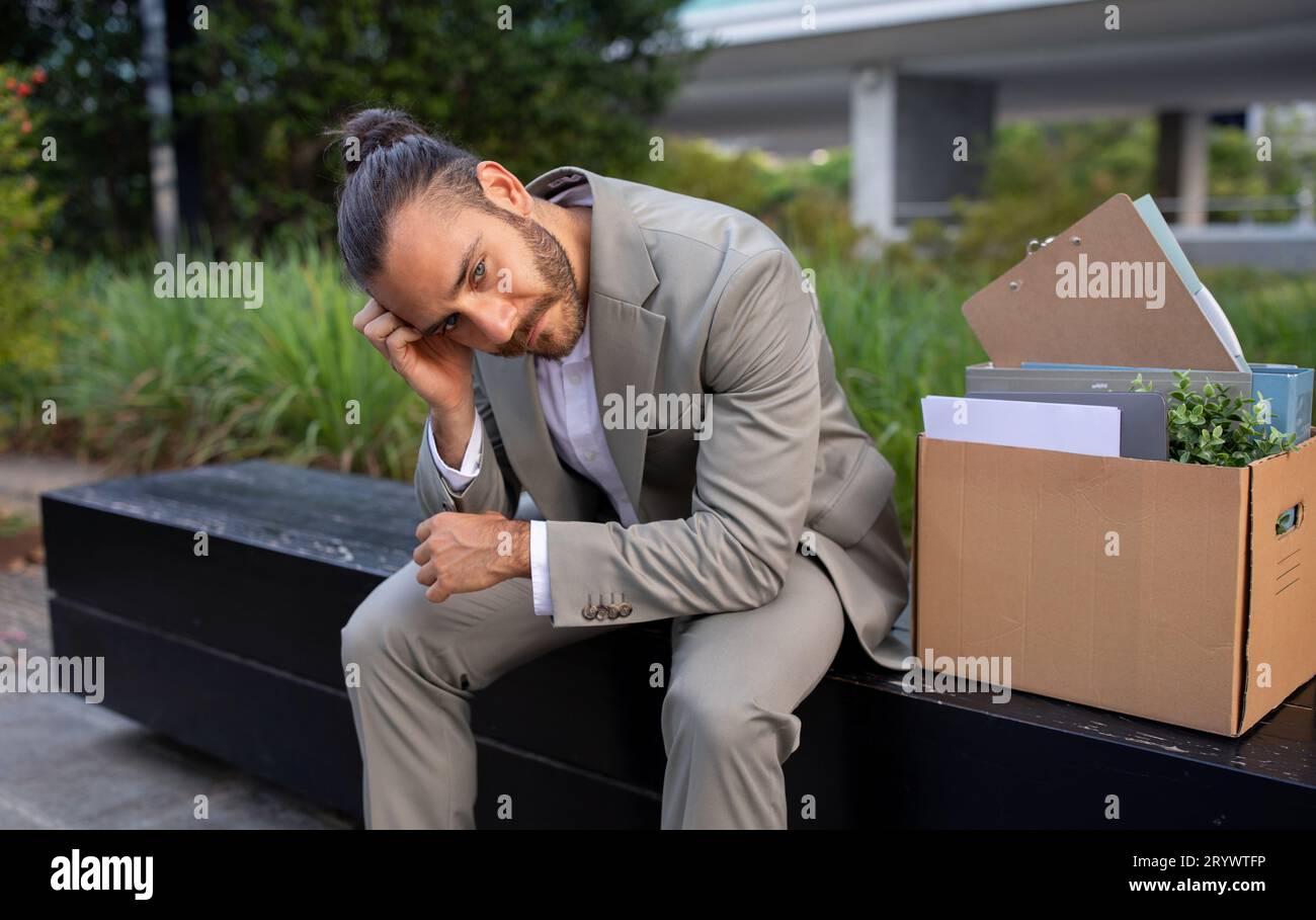 Unemployment concept. Upset office worker sitting with box of belongings outdoors Stock Photo