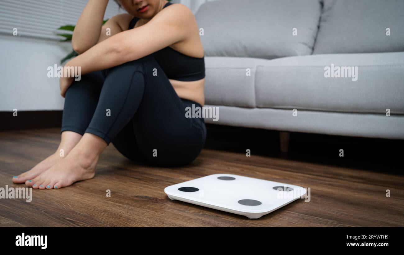 Asian healthy woman bored of dieting Weight loss failÂ  Fat diet and scale sad asian woman Upset on weight scale at home weight Stock Photo