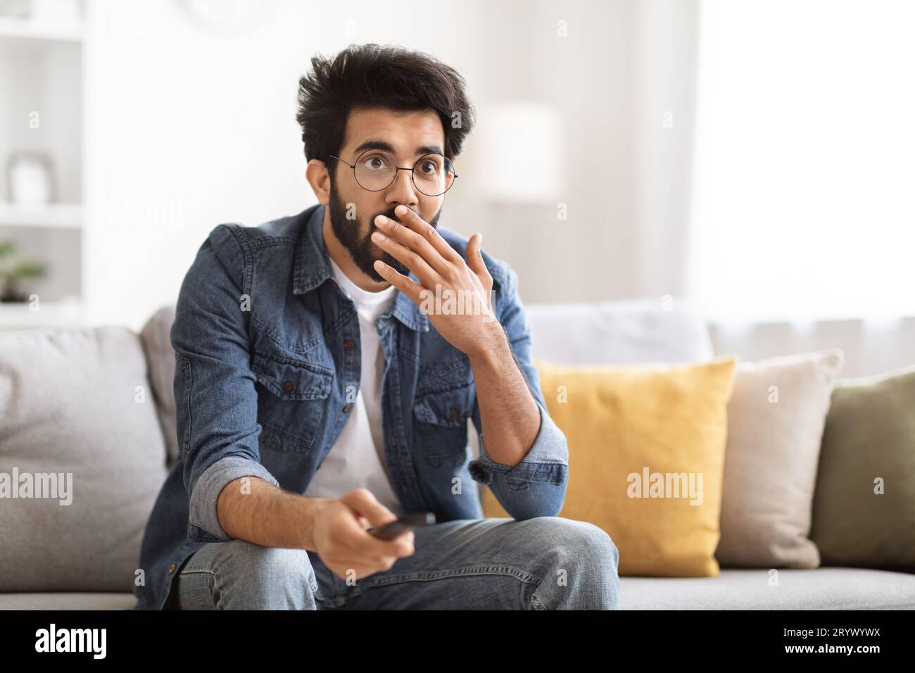 Portrait Of Amazed Indian Guy Holding Remote Controller And Looking At Tv Stock Photo