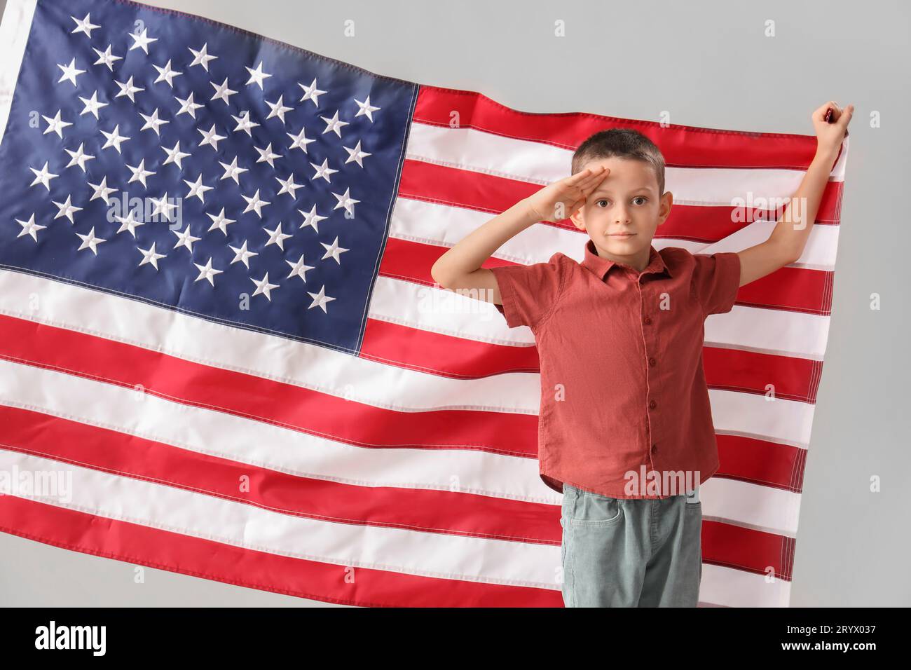 Little boy with USA flag saluting on light background. Veterans Day