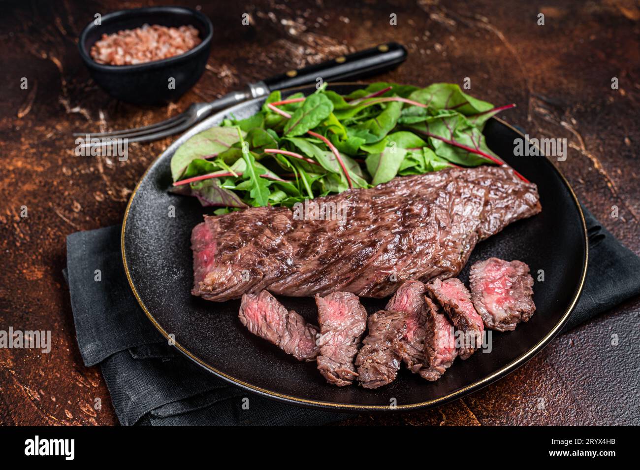 Juicy Grilled Machete skirt beef meat steak on plate with salad. Dark background. Top view. Stock Photo