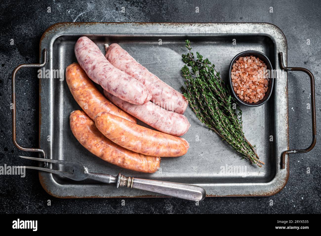 Raw barbecue sausages with spices in kitchen tray. Black background. Top view. Stock Photo