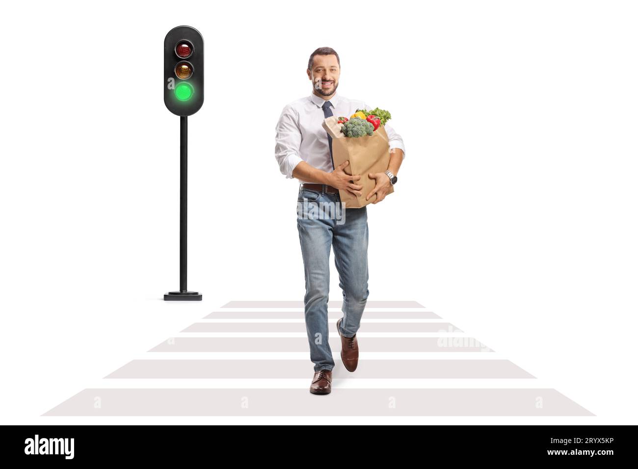 Full length portrait of a smiling professional man walking at a pedestrian and carrying a bag with fruits and vegetables isolated on white background Stock Photo