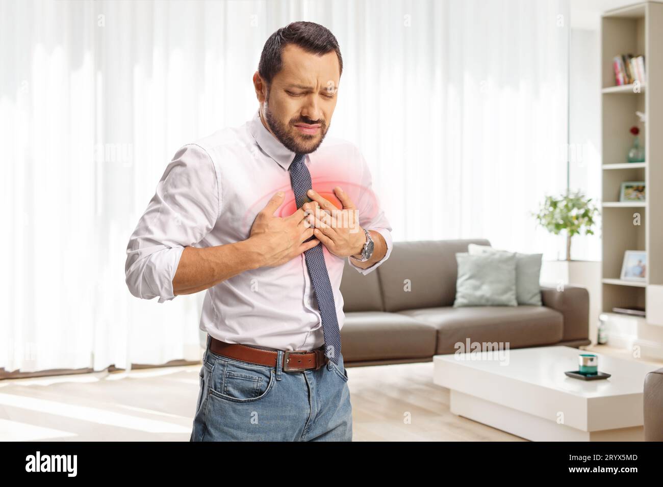 Young man in pain holding his chest and standing in a living room Stock Photo