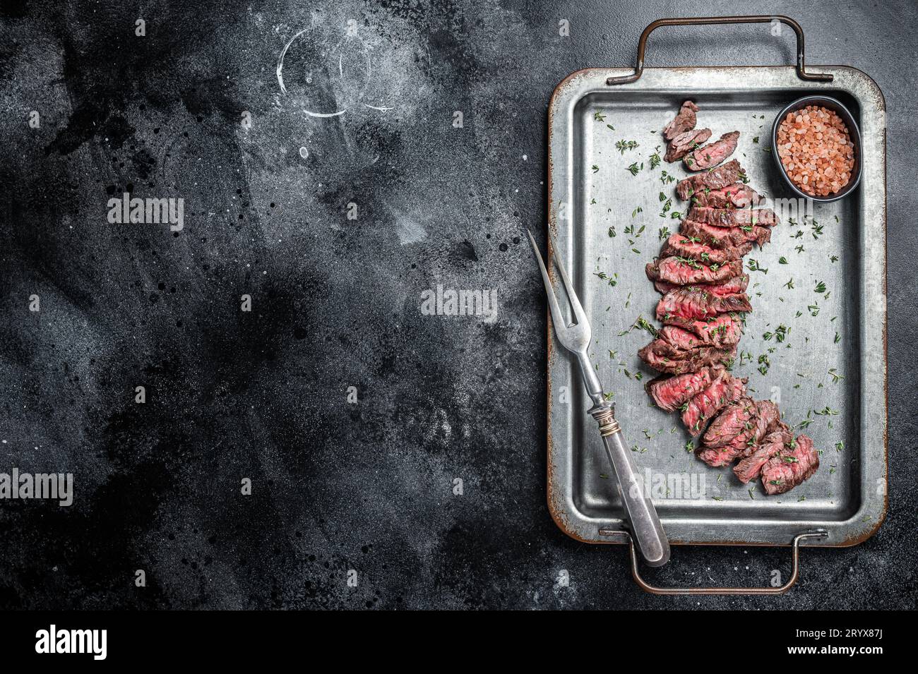 Grilled sliced Machete beef meat steak on steel tray with thyme. Black background. Top view. Copy space. Stock Photo