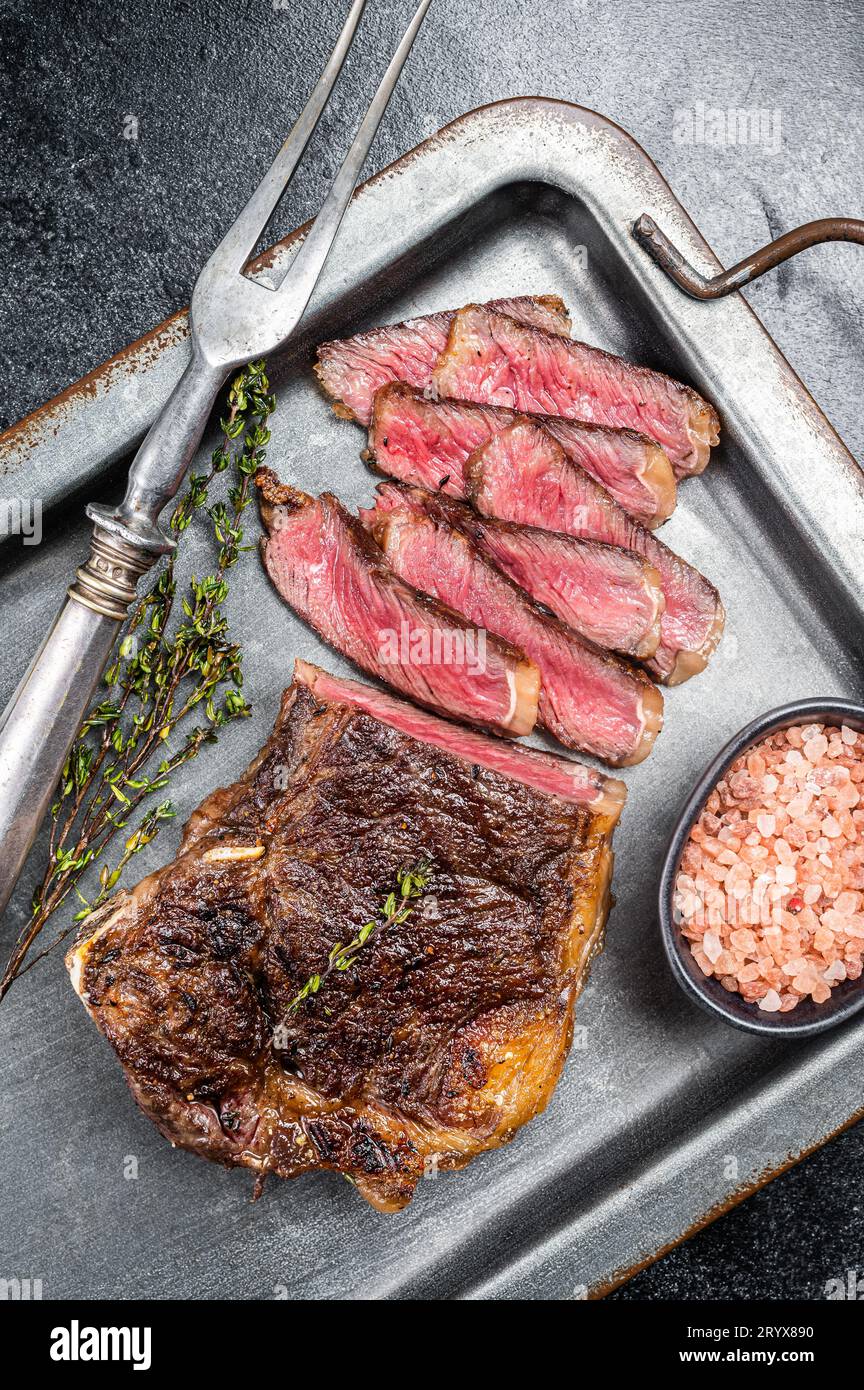 Grilled Wagyu Striploin beef meat steak or new york steak in a steel tray. Black background. Top view. Stock Photo