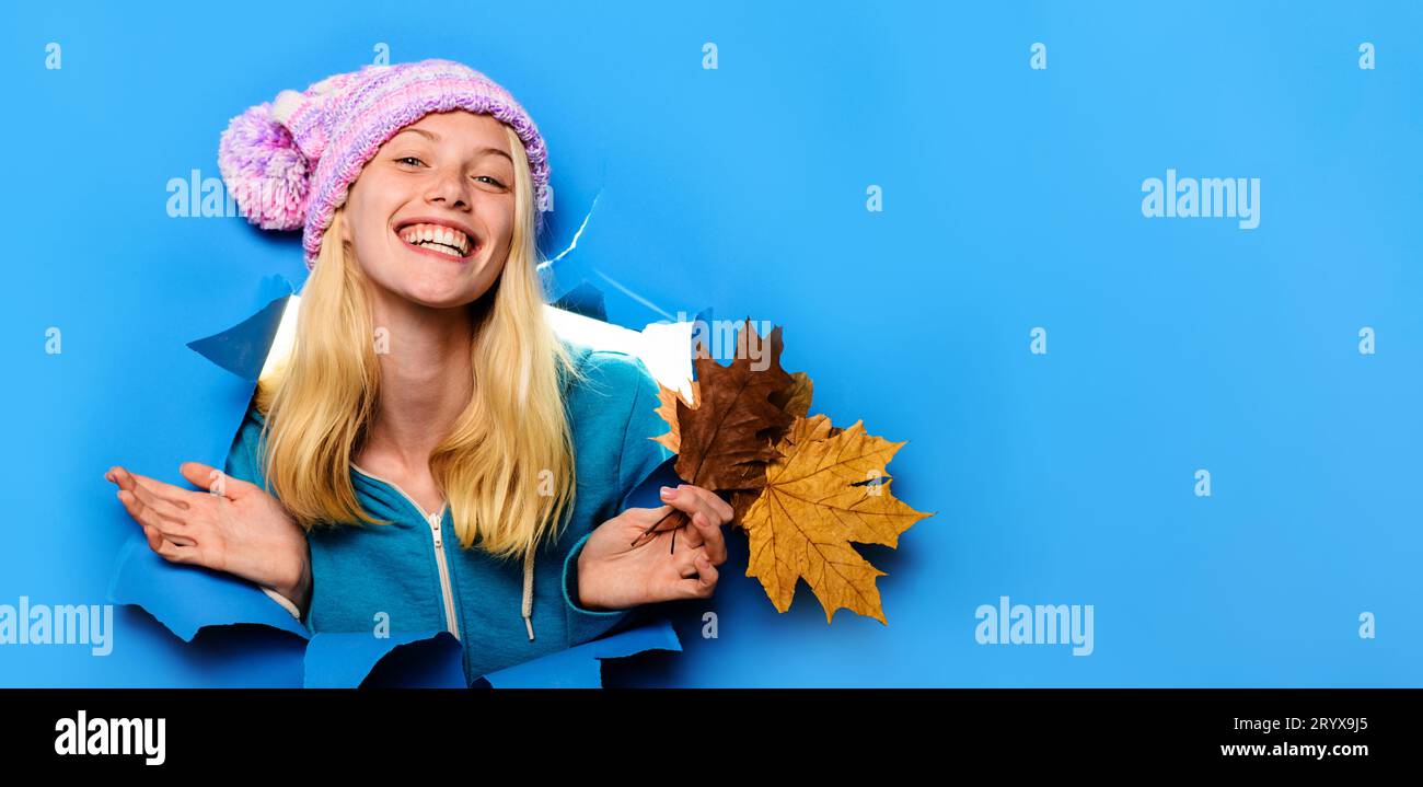 Autumnal mood. Smiling woman in knitted hat with autumn leaves looking through paper hole. Happy girl in autumn wear with fall leaves. Autumn fashion Stock Photo