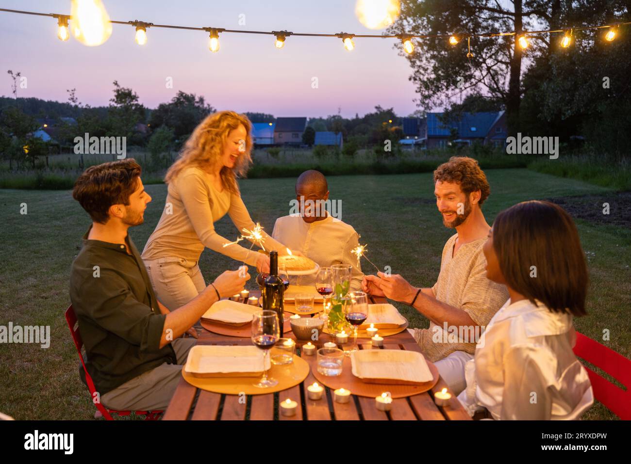 Multiracial group of friends enjoying meal having backyard dinner party - Young people toasting cocktail glasses together- Socia Stock Photo