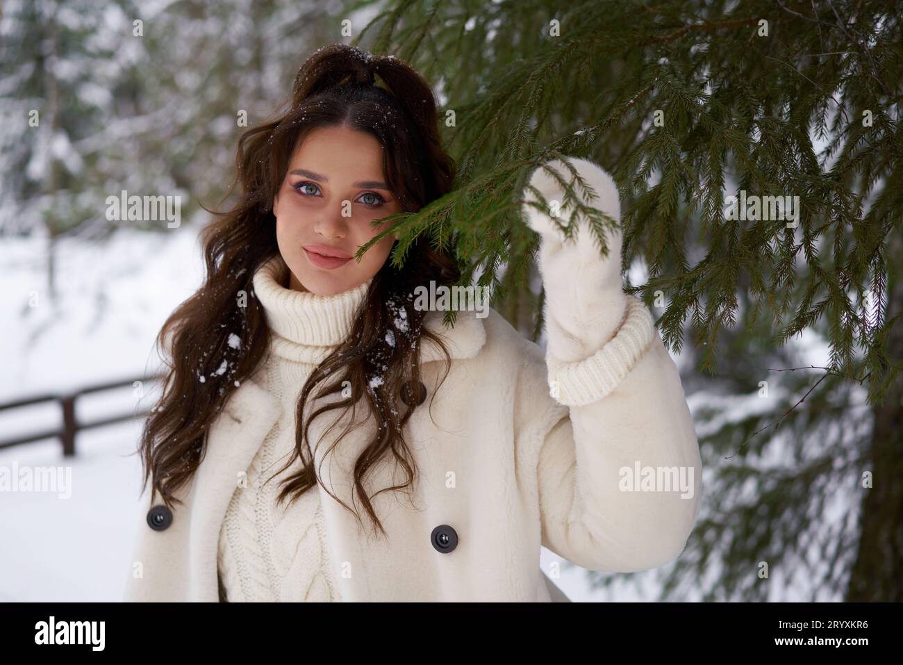 Beautiful woman in white fur posing near spruces in snow. Winter. Stock Photo