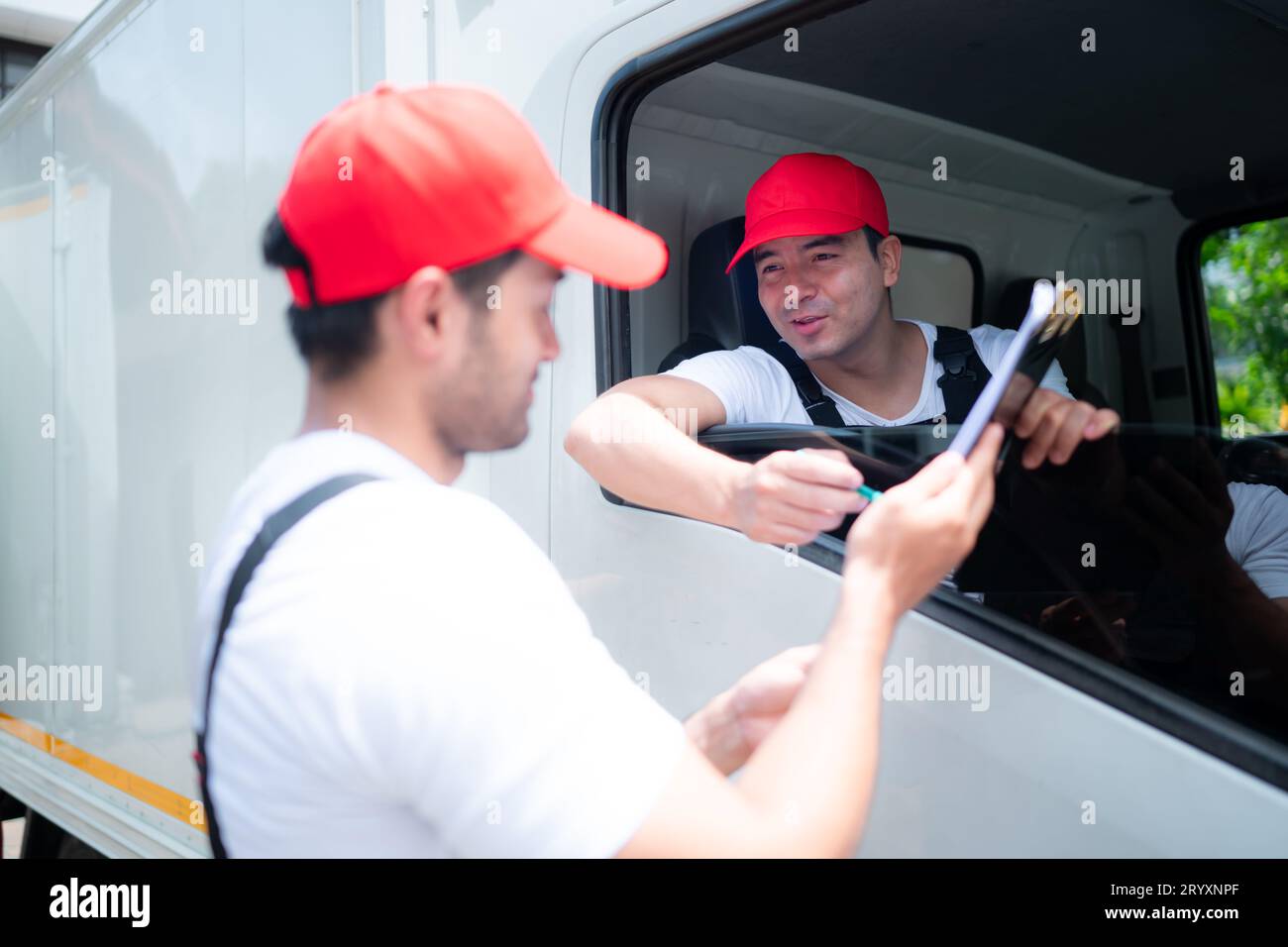 Delivery man in red cap and uniform delivering parcel to recipient - courier service concept Stock Photo