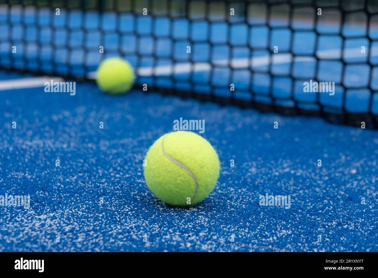 Two balls near the net of a blue padel tennis court, racket sports concept Stock Photo