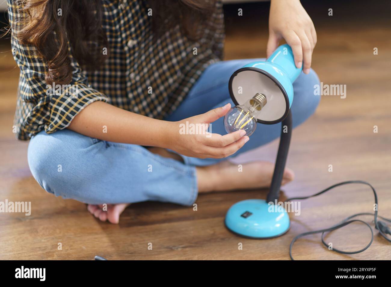 Asian Woman changing light bulb in lamp renovation using equipment to diy repairing light bulb and lamp sitting on the floor at Stock Photo