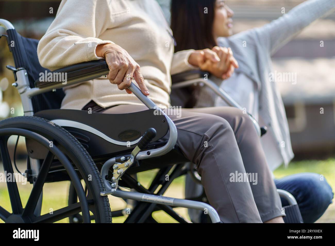 Family relationship Asian senior woman in wheelchair with happy daughter holding caregiver for a hand while spending time togeth Stock Photo