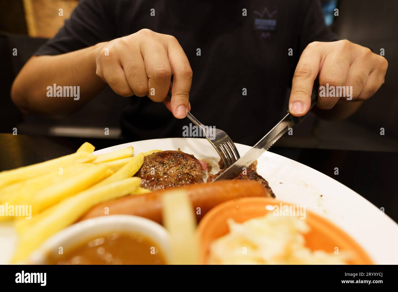 Man eating Grilled Meats stake from plate. hand holding knife and fork