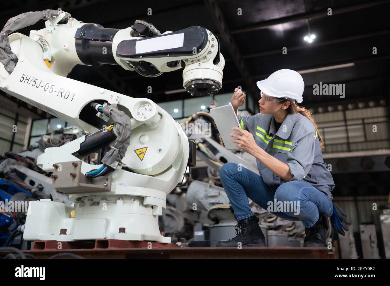 A female engineer installs a program on a robotics arm in a robot warehouse. And test the operation before sending the machine t Stock Photo