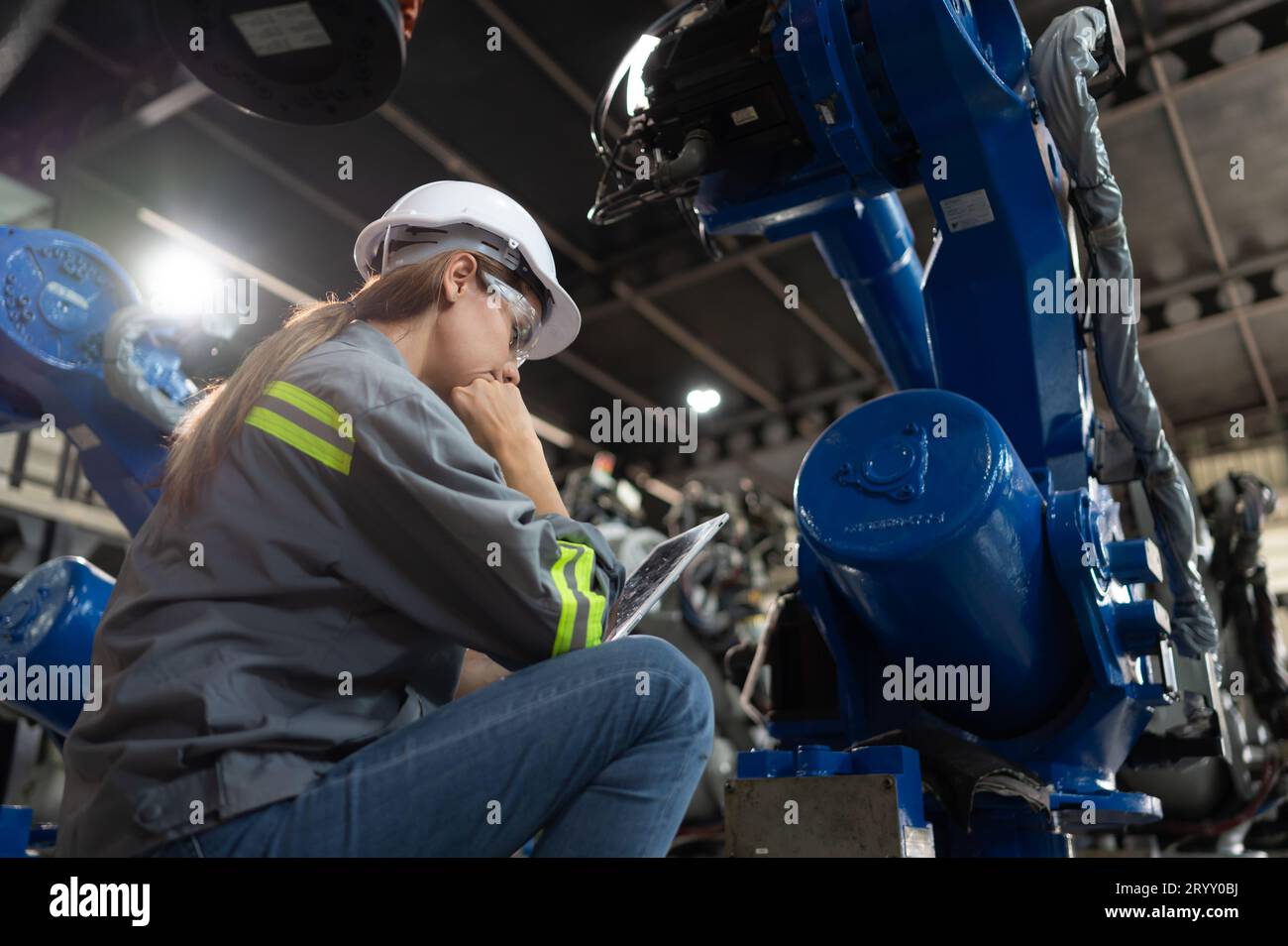 A female engineer installs a program on a robotics arm in a robot warehouse. And test the operation before sending the machine t Stock Photo