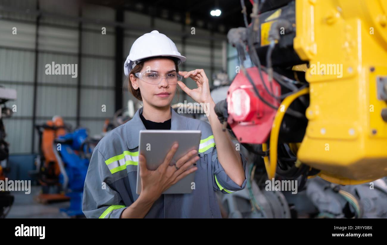 A female engineer installs a program on a robotics arm in a robot warehouse. And test the operation before sending the machine t Stock Photo