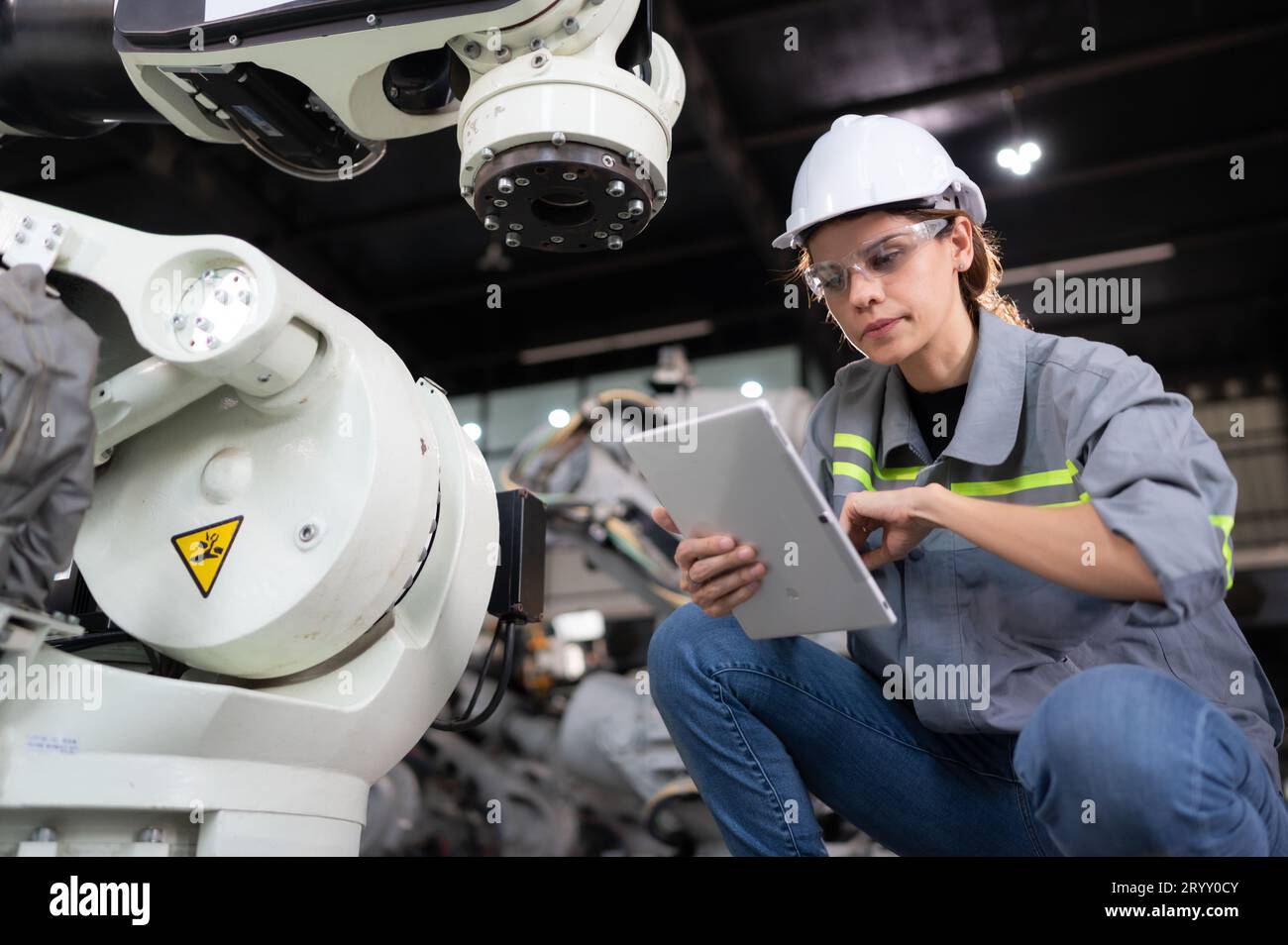 A female engineer installs a program on a robotics arm in a robot warehouse. And test the operation before sending the machine t Stock Photo