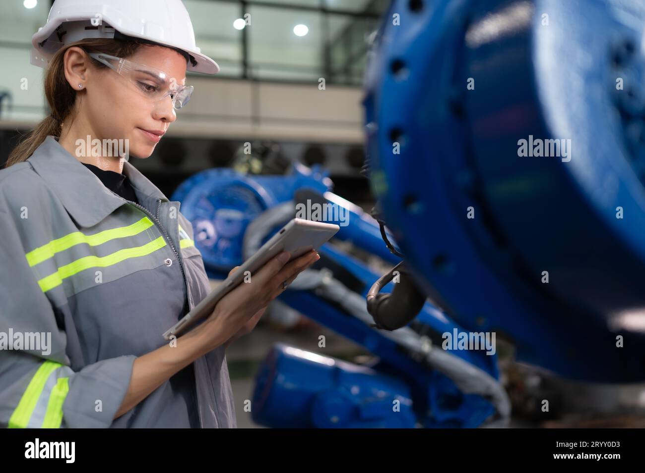 A female engineer installs a program on a robotics arm in a robot warehouse. And test the operation before sending the machine t Stock Photo