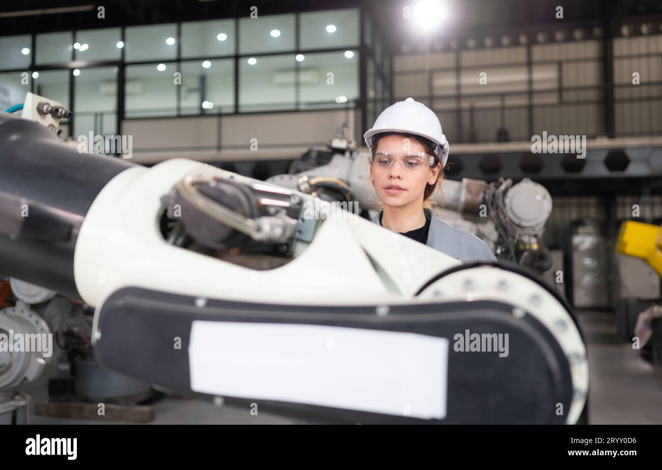 A female engineer installs a program on a robotics arm in a robot warehouse. And test the operation before sending the machine t Stock Photo