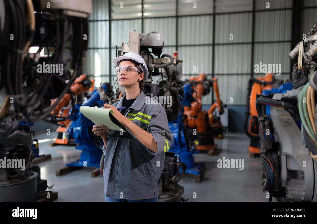A female engineer checking documented items after installing a program on a robotic arm in a robotic warehouse and test the oper Stock Photo