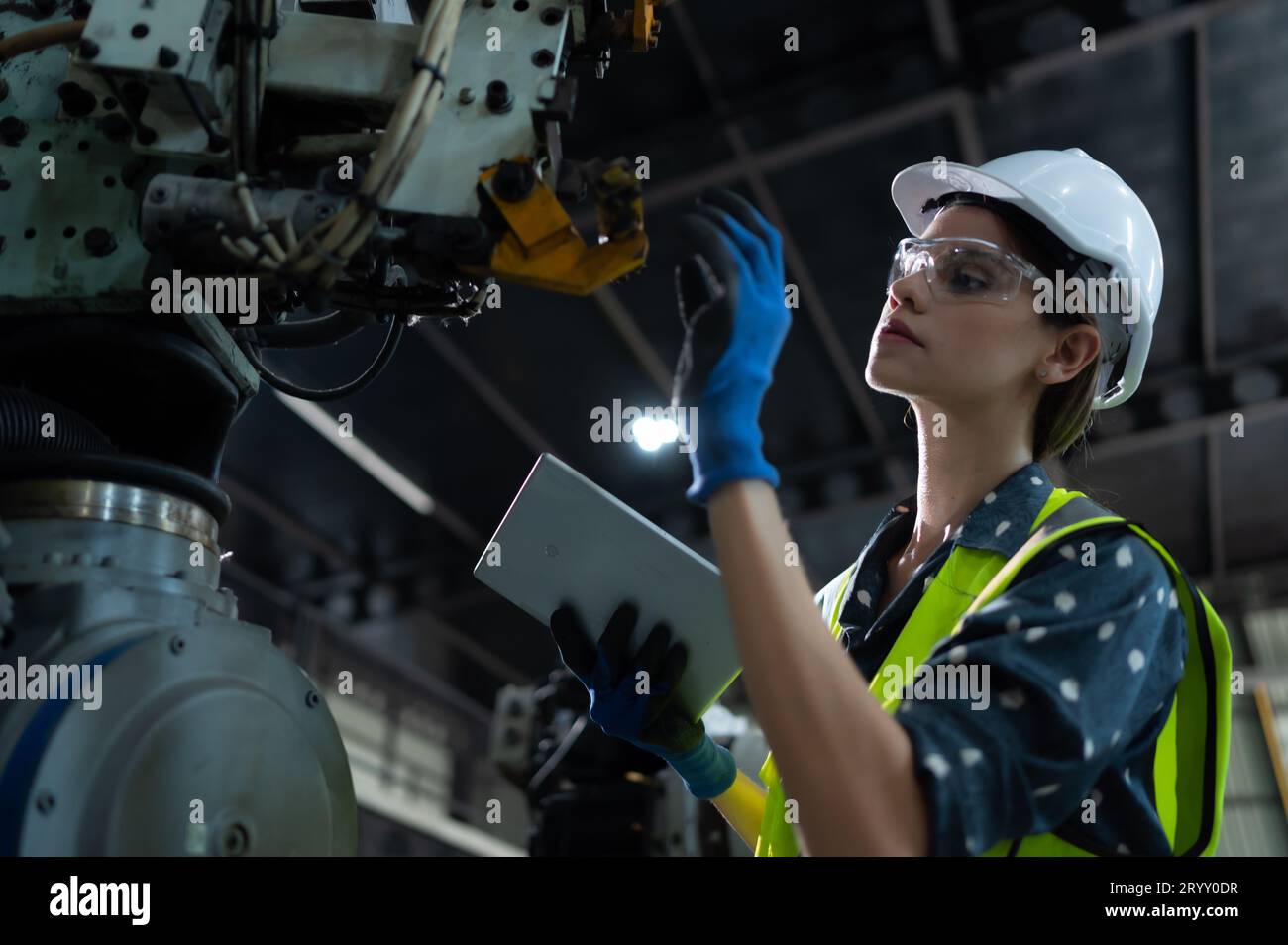 A female engineer installs a program on a robotics arm in a robot warehouse. And test the operation before sending the machine t Stock Photo