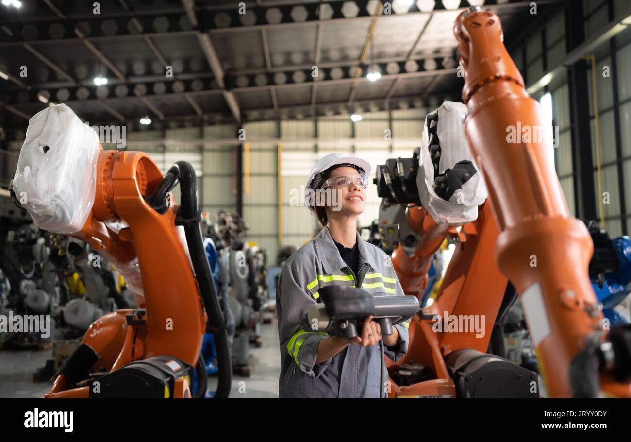 After installing a program on the robotic arm, a female engineer with a robotic arm controller performs a test run. Stock Photo