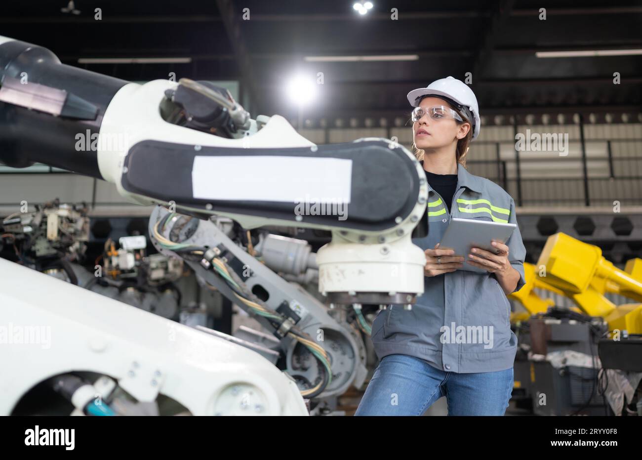 A female engineer installs a program on a robotics arm in a robot warehouse. And test the operation before sending the machine t Stock Photo