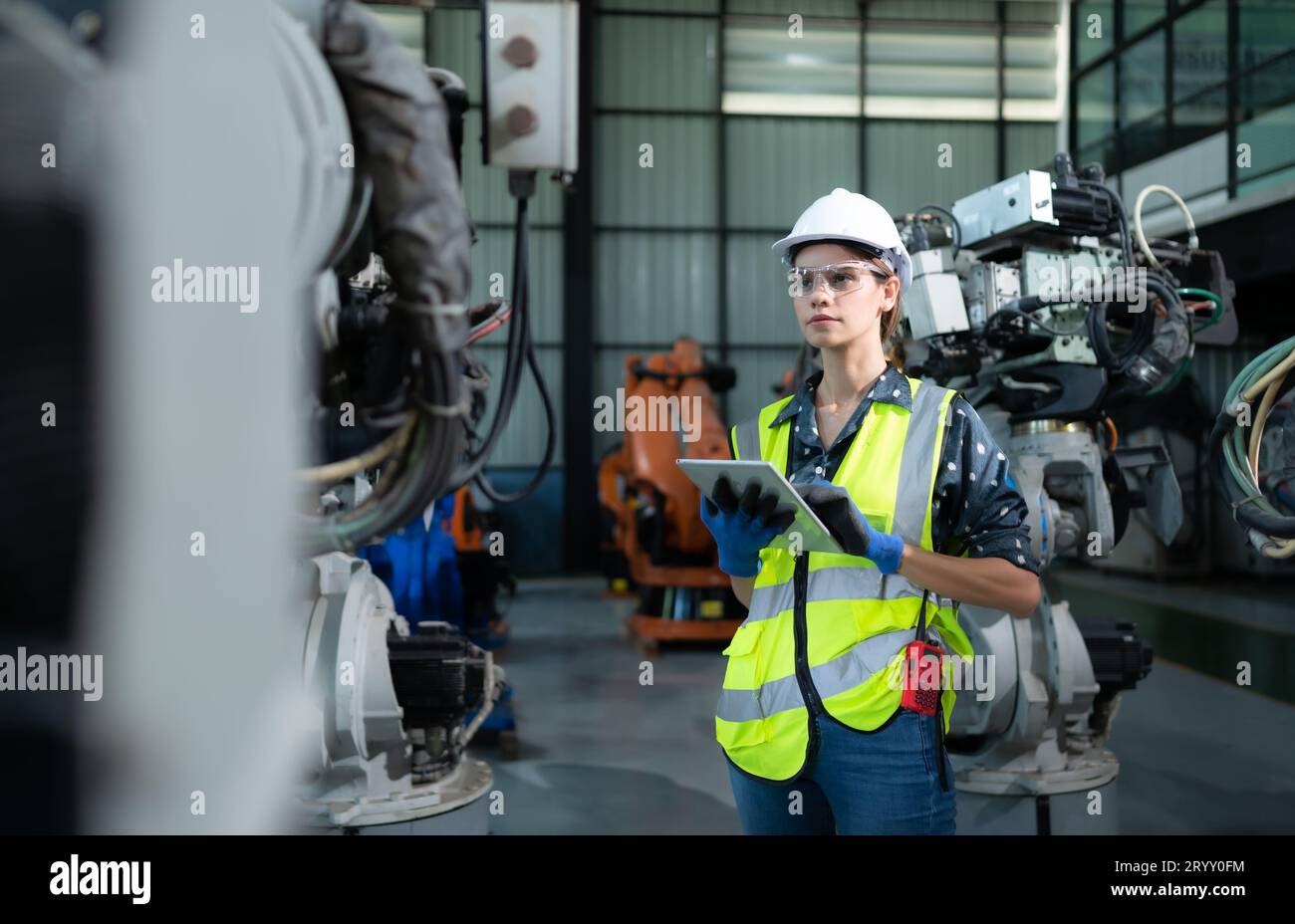 A female engineer installs a program on a robotics arm in a robot warehouse. And test the operation before sending the machine t Stock Photo