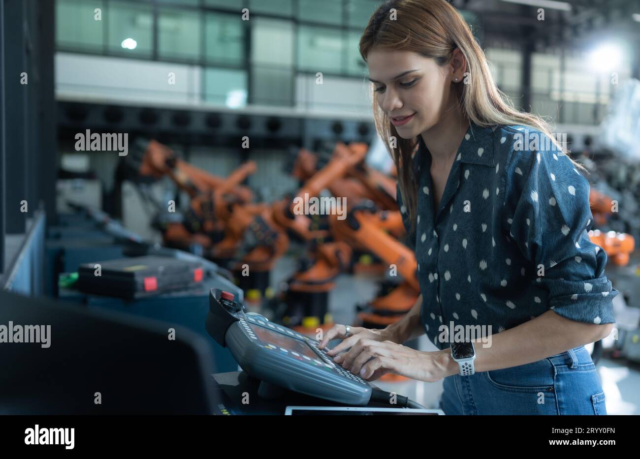 A female engineer installs a program on a robotics arm in a robot warehouse. And test the operation before sending the machine t Stock Photo