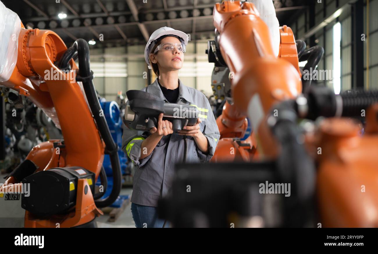 After installing a program on the robotic arm, a female engineer with a robotic arm controller performs a test run. Stock Photo